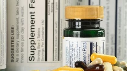 Food supplement bottles and capsules displayed against a background of supplement facts labels.