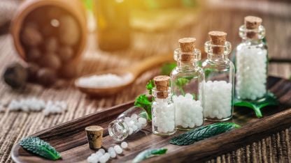 Homeopathic remedy pellets in glass vials arranged on a wooden tray.