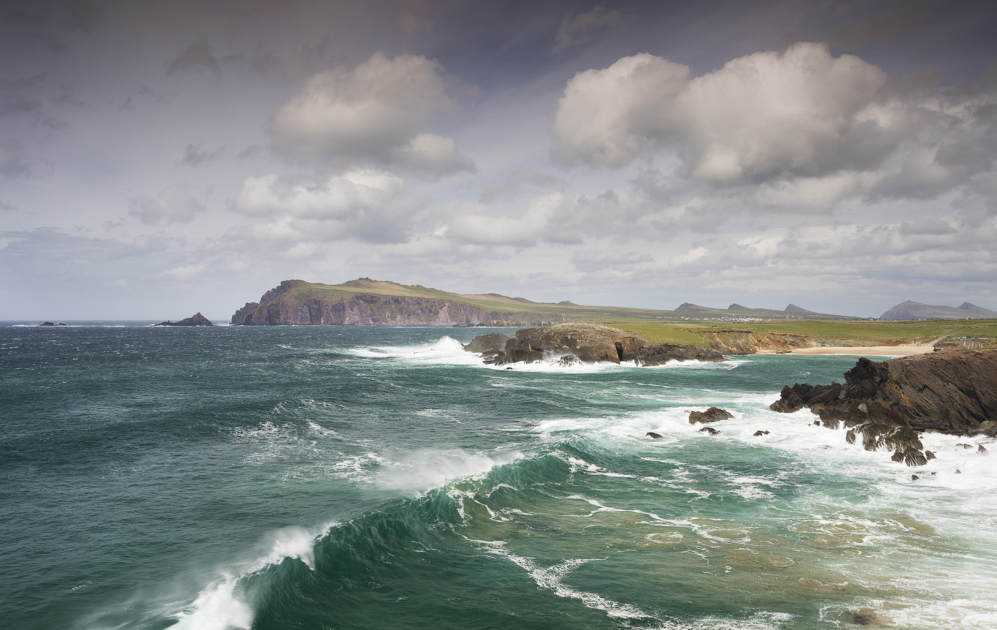 turquoise ocean water with cliffs in the background and waves crashing ashore 